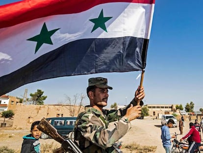 Un soldado del régimen ondea este lunes una bandera de Siria en la entrada occidental de Tal Tamr tras la entrada de las tropas regulares en esta localidad del norte sirio.