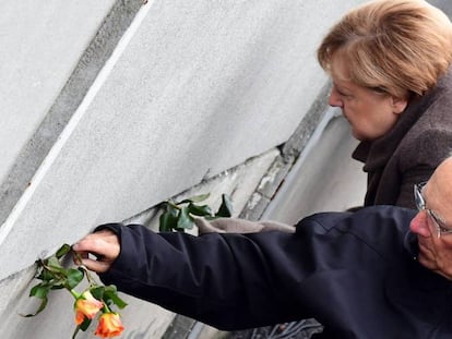 La canciller alemana, Angela Merkel, y el presidente del Bundestag, Wolfgang Schäuble, colocan rosas en una rendija del muro de Berlín durante la celebración del 30º aniversario.
