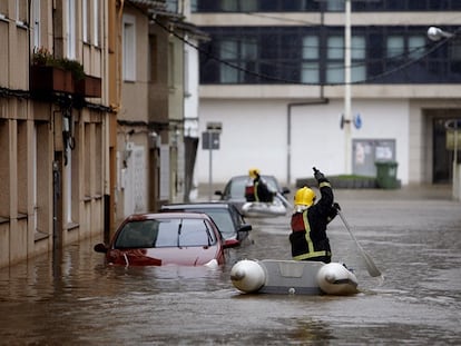 El temporal de lluvia anega pueblos y obliga a rescatar familias en Galicia. Dos bomberos atraviesan en lanchas una calle de Sada.