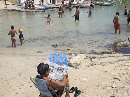 Una mujer lee el periódico en la Cala de Alcafar en Menorca.