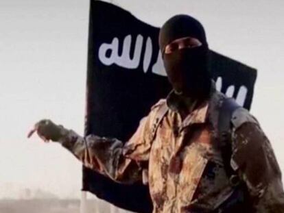 Homem encapuzado diante de uma bandeira do autoproclamado Estado Islâmico.