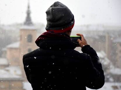 Un turista fotografía una panorámica de Segovia nevada, con la iglesia románica de San Millán al fondo.