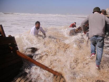 Los empleados del chiringuito El Potito, en Cádiz, intentan salvar el local de los efectos del temporal, con olas de más de 6 metros, en la playa de la Victoria.