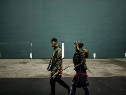 Dos personas caminan delante de un frontón con la bandera vasca, en Hernani.