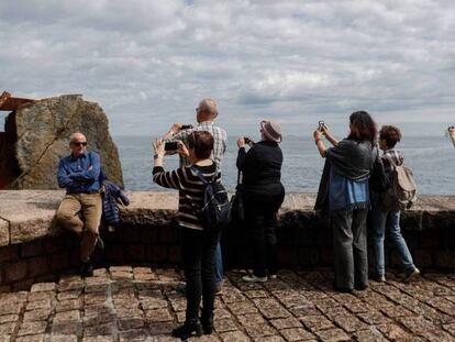 Un grupo de turistas toma fotografías en el Peine del Viento de San Sebastián. En vídeo, se desploman los termómetros en todo el país.