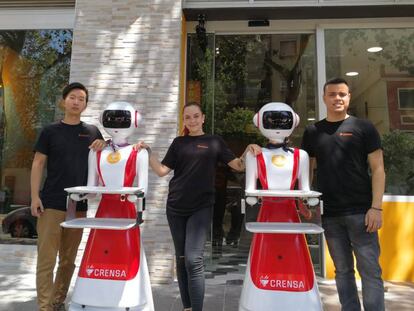 Tres empleados y dos robots del restaurante valenciano Crensa a las puertas del establecimiento. En vídeo, las máquinas en acción.