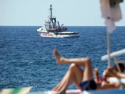 El barco de rescate 'Open Arms', ante las costas de Lampedusa (Italia) mientras unos turistas toman el sol en la isla.