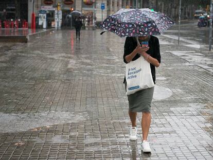 En el vídeo, la DANA se ceba con las islas Baleares. En la foto, una mujer se protege de la lluvia en Barcelona.