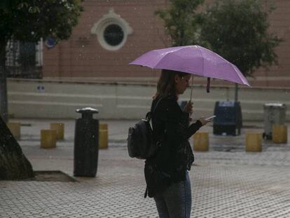 Una mujer se protege de la lluvia en Sevilla. En vídeo, imágenes del temporal.