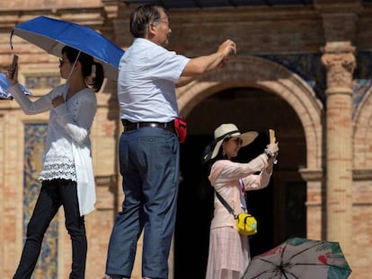 Unos turistas asiáticos se protegen del sol mientras toman fotografías en la plaza de España de Sevilla.