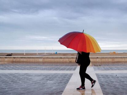 Una persona pasea por la playa de la Malvarrosa, en Valencia, protegida con un paraguas el domingo por la mañana.