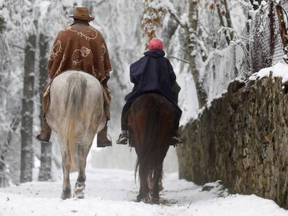 Dos personas pasean a caballo por un paisaje nevado este viernes por la localidad de O Cebreiro (Lugo). En vídeo, cae la primera gran nevada en España.