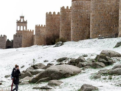Una mujer camina esta mañana junto a la nevada muralla de Ávila.