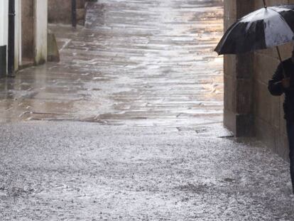 Un hombre se cubre de la lluvia con un paraguas mientras pasea por una calle de Santiago de Compostela. En vídeo, los efectos de las lluvias y la previsión del tiempo.