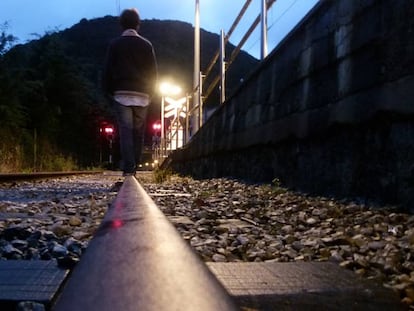 Un adolescente camina por una vía del tren. En vídeo, reportaje sobre el teléfono de atención al suicidio.