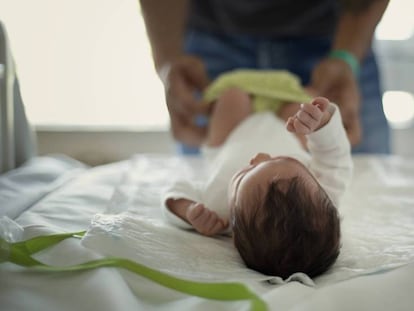 Un padre cambia los pañales de su hija recién nacida en el hospital Sant Pau de Barcelona. En vídeo, declaraciones de diferentes padres ante la nueva normativa.