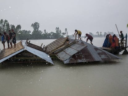 Varios afectados por las inundaciones cargan trozos de sus casas en una barca en Kurigram, Bangladesh, el pasado 27 de julio. En vídeo, el reportaje.