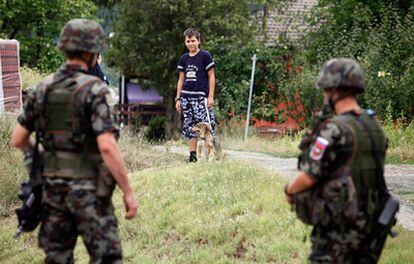 Un niño serbiokosovar observa a soldados eslovenos de la KFOR mientras pasea su perro por la localidad de Rudare.