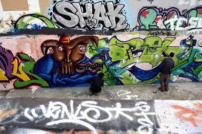 Dos personas hacen una pintada sobre un muro en el parque de San Isidro.