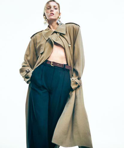 Anja Rubik is wearing a trench coat, pants, earrings and belt, all by SAINT LAURENT BY ANTHONY VACCARELLO.