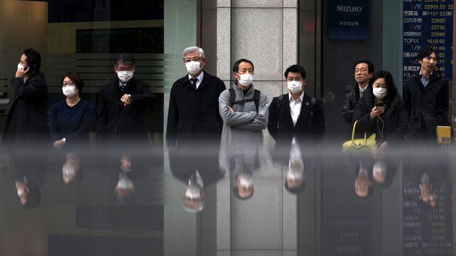 TOKYO, JAPAN - FEBRUARY 25: Pedestrians wearing face masks wait to cross a road in front of a monitor displaying stock information outside a securities firm on February 25 in Tokyo, Japan. The Nikkei index dropped more than 3.5 percent at the open on Monday as global concerns grow about the economic impact of the Coronavirus. (Photo by Tomohiro Ohsumi/Getty Images)