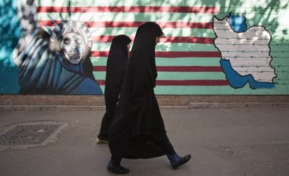 Mujeres iraníes caminan frente a una pintada contraria a Estados Unidos en Teherán.
