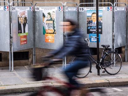 Una mujer pasea en bicicleta junto a varios carteles electorales en una calle de París, Francia.