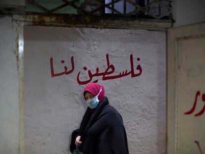 Una mujer camina entre las callejuelas del campo de refugiados de Chatila. A su espalda, se puede leer la frase "Palestina nuestra", escrita en árabe.