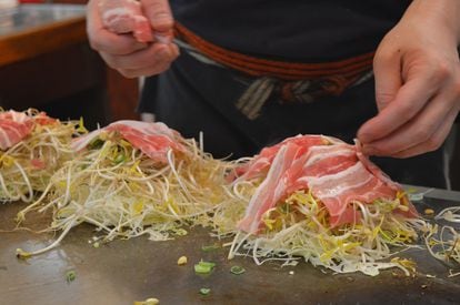 The cook arranges thin layers of meat during the okonomiyaki making process.