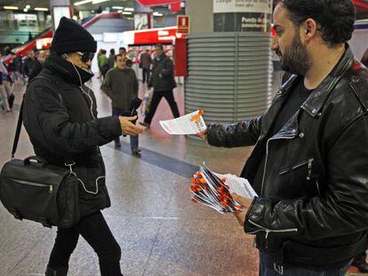 Uno de los voluntarios de la Oficina Precaria entrega folletos con lazos naranjas en Atocha.