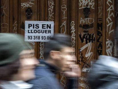 Viandantes frente a un portal con un anuncio inmobiliario, en el distrito barcelonés de Ciutat Vella.