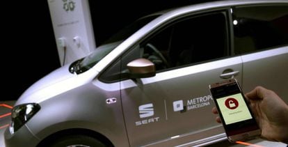 Una persona sostiene un teléfono móvil frente a un coche de Seat.