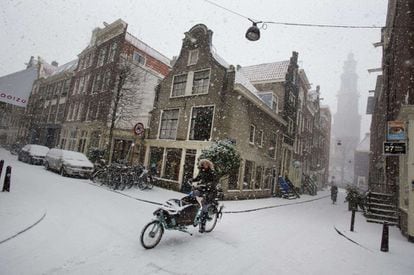 Una mujer avanza con una bicicleta por una calle nevada de Amsterdam.