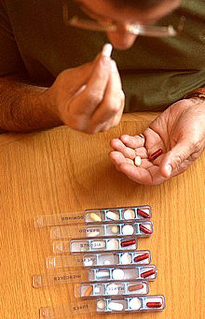 Un polimedicado coge una píldora de un pastillero.