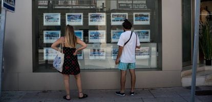 Dos personas observan inmuebles en alquiler y en venta en un escaparate de una inmobiliaria ubicada en Palma de Mallorca