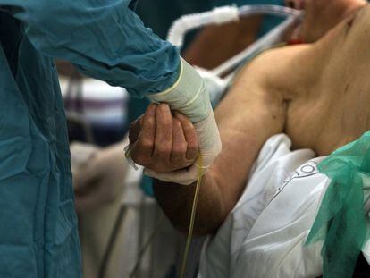 Un enfermero sostiene la mano de un paciente en el hospital Cl&iacute;nico de Barcelona.