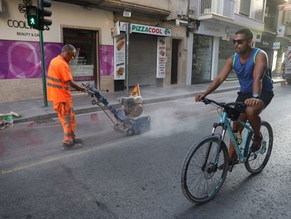 Un ciclista pasa por la calzada de una calle de Elche mientras los operarios eliminan las señales del carril bici.