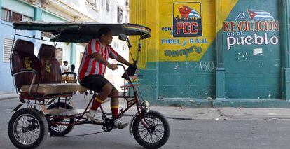 Un hombre conduce un bicitaxi frente a un cartel alusivo el Partido Comunista de Cuba (PCC), en La Habana (Cuba).