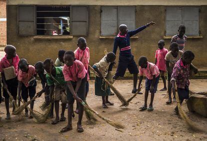 En las escuelas ugandesas los niños llegan a clase mucho antes de que arranque la lección del maestro. Desde las 7.30 de la mañana, distribuidos en pequeños grupos, los chavales del colegio Odu, en Adjumani, se emplean a fondo durante media hora en la limpieza de las letrinas y los vestuarios, con ayuda del agua que cogen de cuatro fuentes y que mezclan, cuando hay, con polvo de detergente. Además, cargan en carretillas la hojarasca caída de los árboles durante la madrugada. Barren con unas rudimentarias escobas hechas con ramas secas de matorral. Denish (en el centro de la imagen, con el brazo en alto) dirige y coordina los trabajos. Todos cumplen sus órdenes diligentemente y sin rechistar.