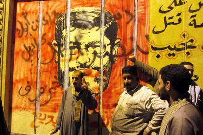 Tres personas frente a un mural que muestra al presidente egipcio Mohamed Morsi.