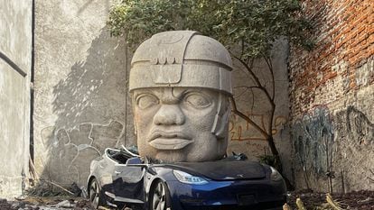 La réplica de una cabeza olmeca aplasta un auto Tesla, en una obra de arte de Chavis Mármol.
