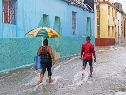 Dos personas caminan bajo la lluvia en una calle de Santiago de Cuba.