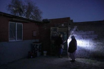 Dos mujeres se ayudan de una linterna para moverse por el exterior de su casa. Los vecinos culpan a la empresa Naturgy de tenerlos sin suministro eléctrico desde hace dos meses. La compañía niega que realice cortes de luz y señala que se deben a la subida de tensión por las plantaciones de marihuana