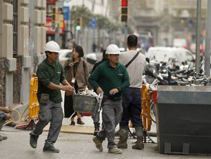 Dos trabajadores echan escombros en un contenedor en una calle de Barcelona.