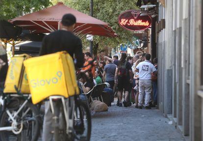 Two Glovo delivery men (or 'riders') wait to take an order on a street in the center of Madrid.  