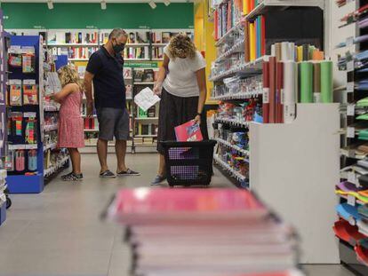 Una pareja acompañados por una niña realizan una compra de material escolar en una papelería de Valéncia.