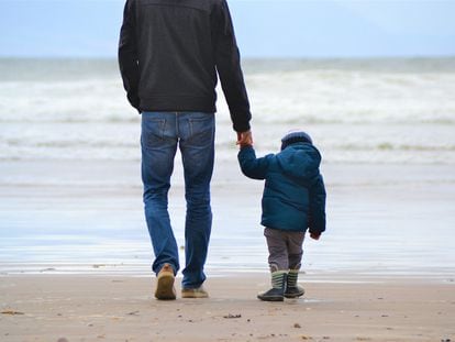 Un padre camina con su hijo por la playa.