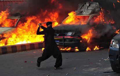 Una manifestante junto a unos cohes de policía quemados en la ciudad pakistaní de Harachi.