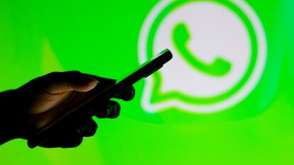 Un usuario maneja un móvil frente al logo de WhatsApp.