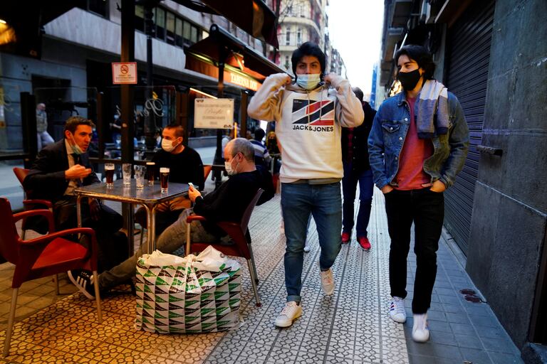 Varios jóvenes con mascarilla pasan ante los clientes de un bar en el centro de Bilbao.